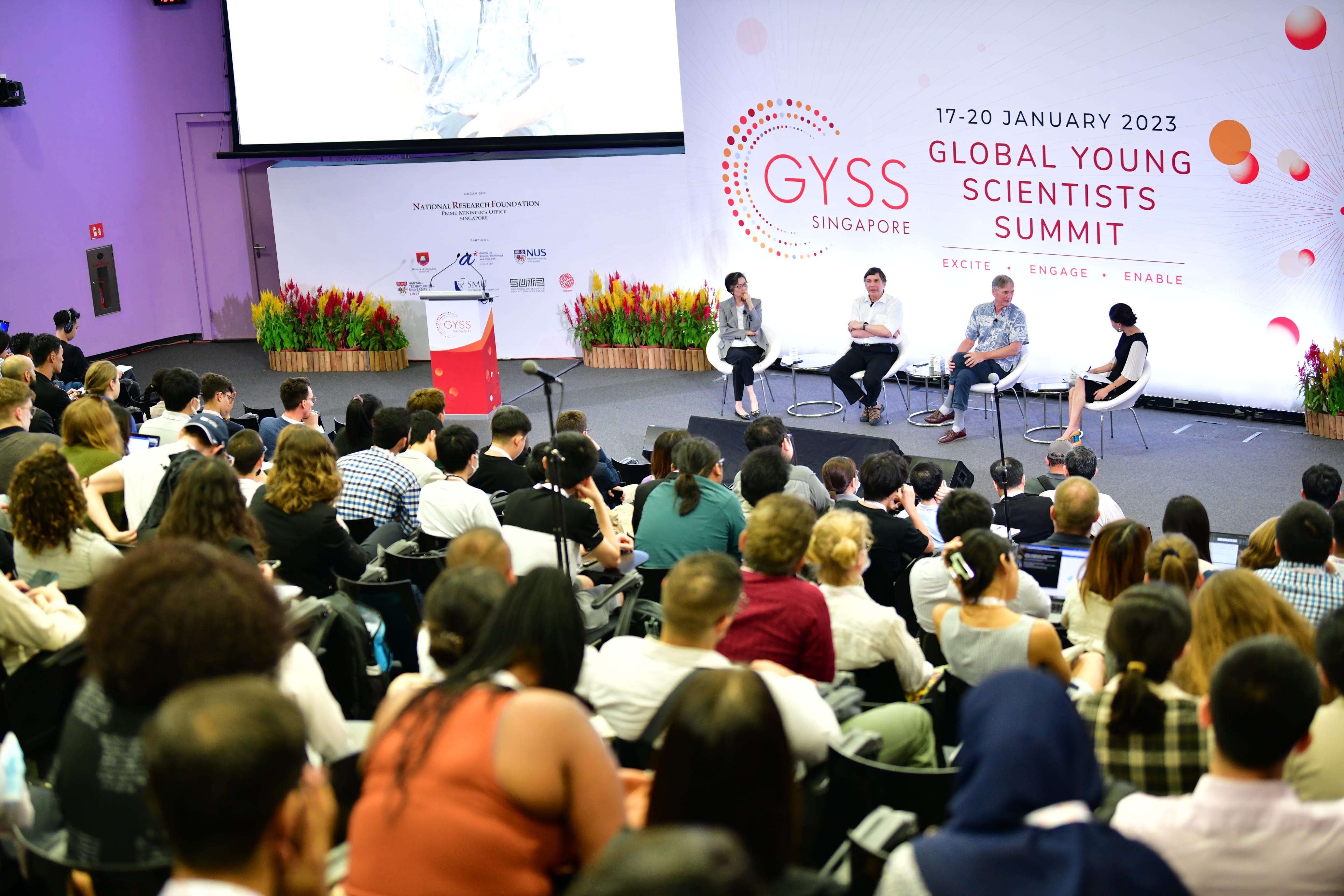 A packed auditorium at the Global Young Scientists Summit Singapore, January 2023, with four panelists seated on stage.